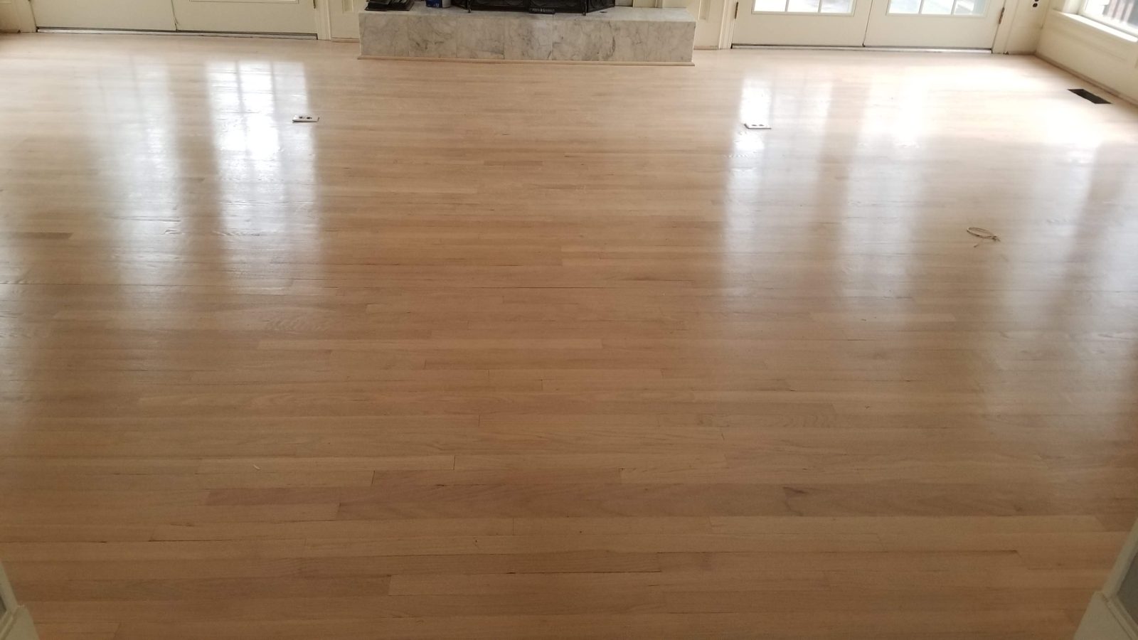 Freshly refinished hardwood floor in a bright room with white French doors and a marble fireplace
